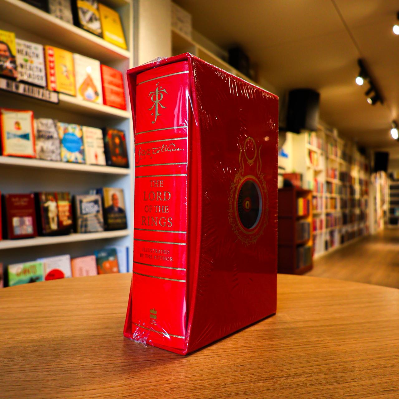 Red book titled 'The Lord of the Rings' on a wooden table with a blurred bookshelf background